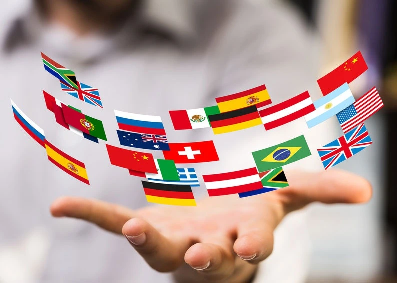 Über 20 Länderflaggen der Welt schweben über einer ausgestreckten Hand. Die Flaggen sind leicht in einem leichten Halbkreis angeordnet und überlappen sich teilweise. Es zeigt eine nicht abgeschlossene Liste von Sprachen, die die Sprachschule anbietet.